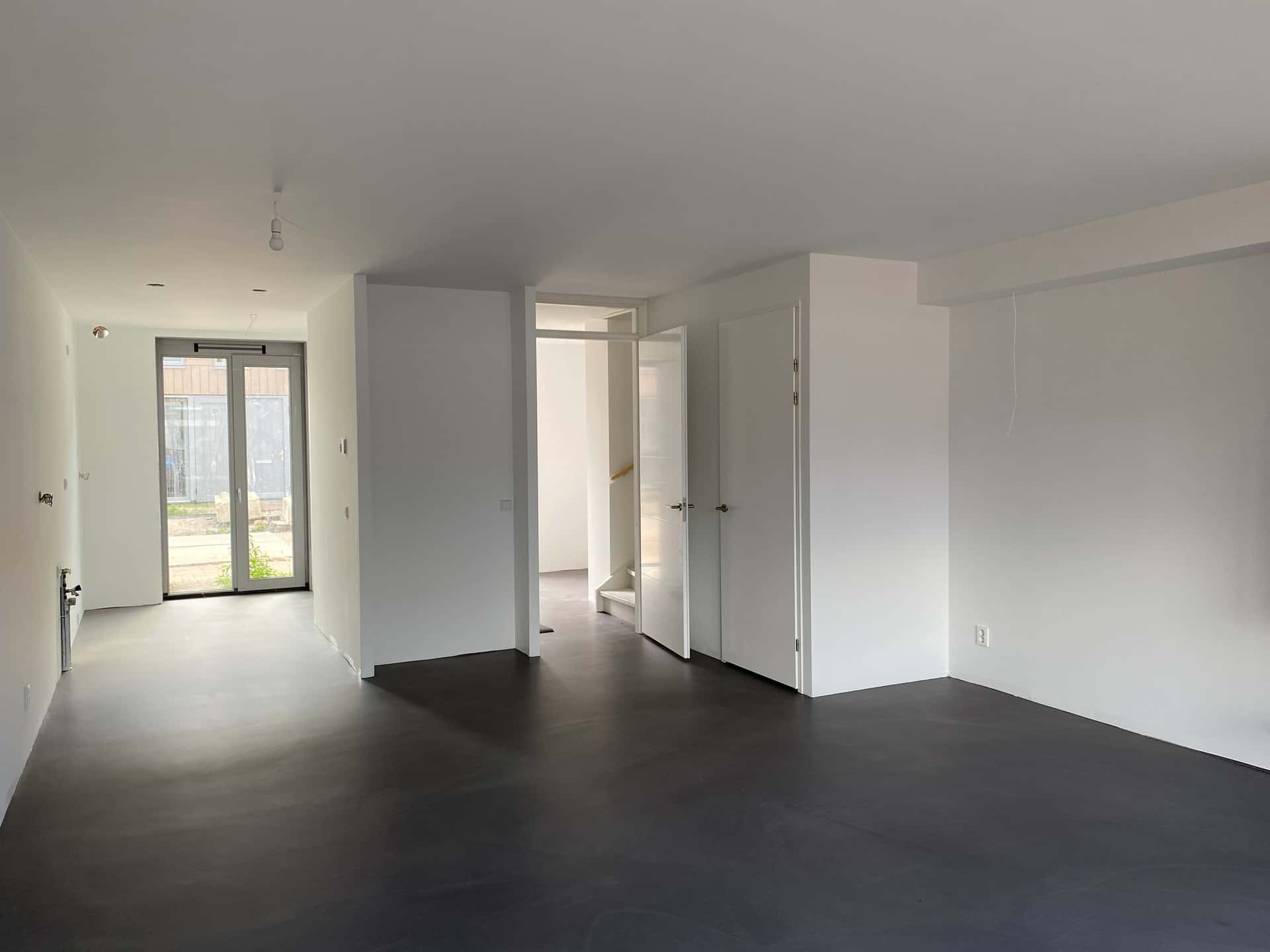 Opgeleverde nieuwbouw-woonkamer met tuindeuren en donkergrijze gietvloer